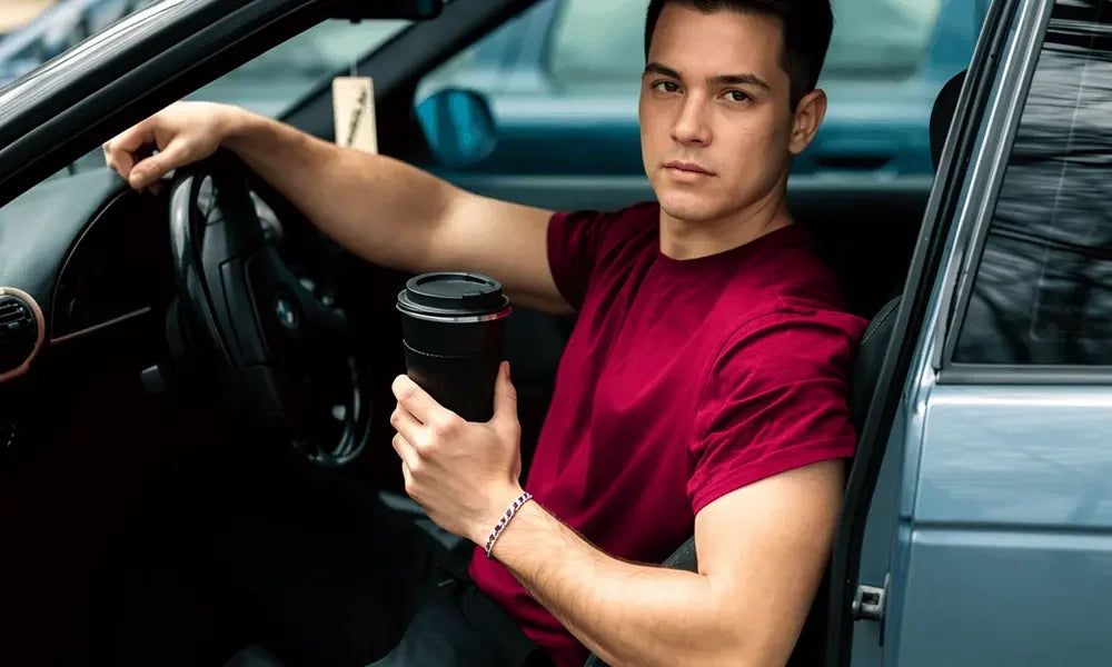 Man in red shirt holding coffee cup while sitting in car