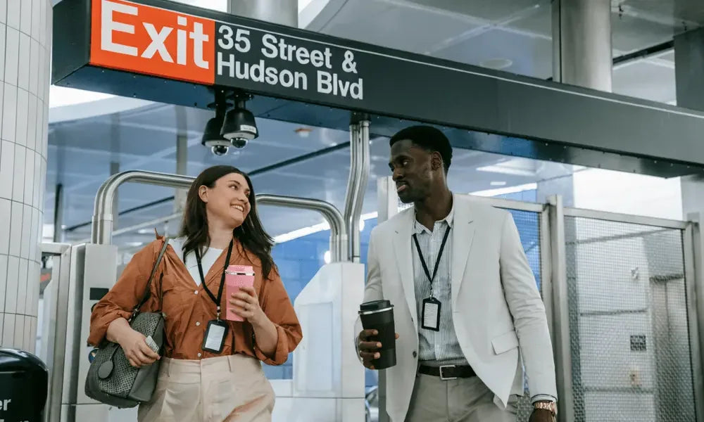 Two professionals walking near Exit 35 Street & Hudson Blvd, holding coffee cups in a modern transit station.